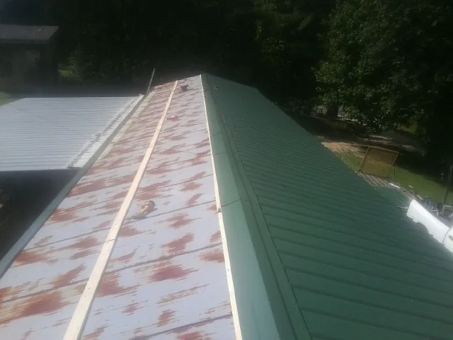 Old rusted panels beside newly installed green metal roofing — Wind Damage Roof Repair by Roofing Brothers in Raymond
